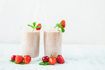 two glasses of smoothies made from milk, strawberries, banana, cherries, decorated with mint on bright white background Concept healthy lifestyle, diet, tasty Copy space