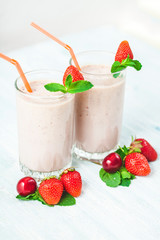 two glasses of smoothies made from milk, strawberries, banana, cherries, decorated with mint on bright white background Concept healthy lifestyle, diet, tasty Close up