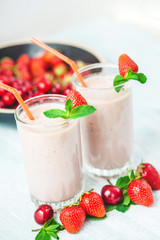 two glasses of smoothies made from milk, strawberries, banana, cherries, decorated with mint on bright white background Concept healthy lifestyle, diet, tasty Close up