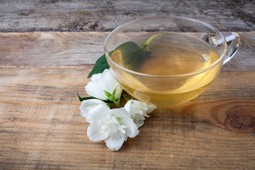 Glass cup of tea with jasmine flowers on wooden background.