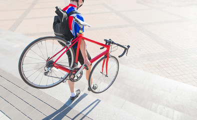 Man cyclist wearing a bicycle down the stairs. A cyclist in sportswear, a helmet and a backpack on his back descends from the ladder with a red bicycle in his hands. Sports concept