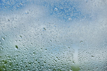 drops of summer rain on the window glass of fresh blue and white clouds background texture