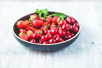 Black plate with cherries, strawberries and mint. Summer concept. Copy space