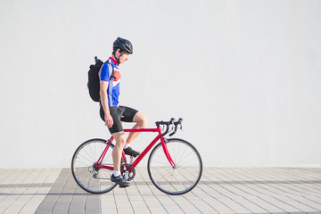Fototapeta premium Athlete cyclist in cycling clothes and a helmet riding a bike without hands on the background of a light wall. Sports concept. Man with a bicycle on the flush wall.
