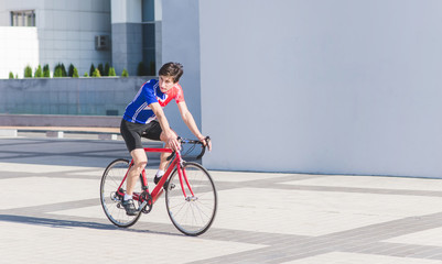 Man cyclist in sportswear rides a red road bike on the background of buildings and a white wall for copyspace. Sports concept