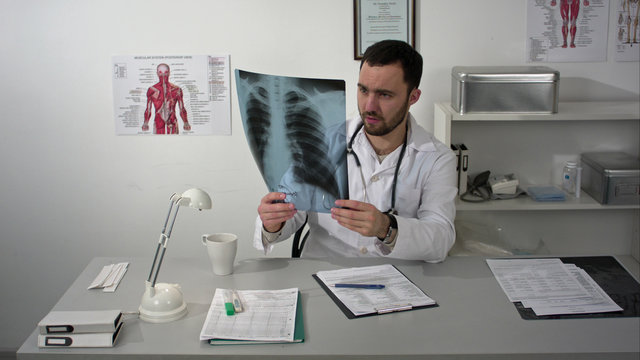 Serious medical doctor sitting at table and looking patients x-ray