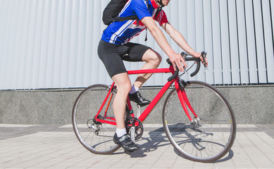 Close-up portrait of a cyclist in red sportswear riding a red bike against a background of gray wall. Bicycle and legs close-up. Sports concept