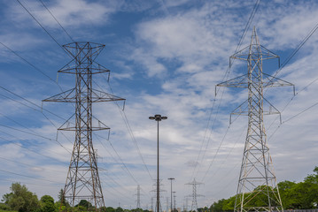 Electric poles and power lines in a suburban area at midday with a blue cloudy sky in the background