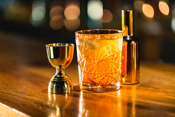 Three colorful cocktails in large glasses in a classic bar environment with dozens of blurry liquor bottles in the background.