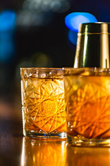 Three colorful cocktails in large glasses in a classic bar environment with dozens of blurry liquor...
