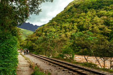 Fototapeta na wymiar Group of backpackers walk towards Machu Picchu on the railway tracks along the Vilcanota River (Urubamba)