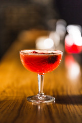 Three colorful cocktails in large glasses in a classic bar environment with dozens of blurry liquor bottles in the background.