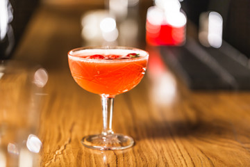 Three colorful cocktails in large glasses in a classic bar environment with dozens of blurry liquor bottles in the background.