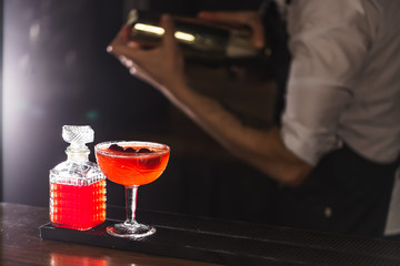 Three colorful cocktails in large glasses in a classic bar environment with dozens of blurry liquor...