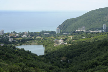 Fototapeta na wymiar View of a small resort town Krasnokamenka and a lake situated at a foothill of a mountain, sea in the background. June 11, 2017. Crimea