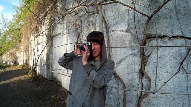 Portrait of beautiful smiling brunette girl making photographs with vintage film camera standing in front of the concrete wall with dry vine 9