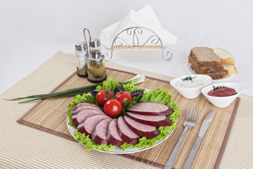 Smoked sausage with tomatoes and lettuce leaves on a plate.