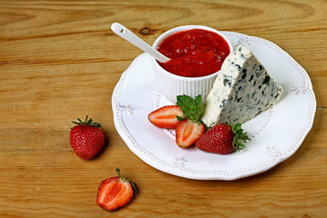Cheese with a noble blue mold on plate with strawberries and with strawberry sauce, mint, on a wooden background. Top view with copy space. set