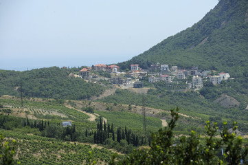 Fototapeta na wymiar View of a small resort town Krasnokamenka situated at a foothill of a mountain, sea in the background. June 11, 2017. Crimea