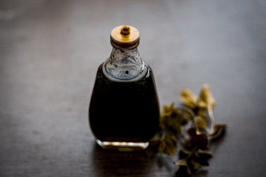 Ayurevedic essence or oil of holy basil or tulsi in a transparent bottle with some fresh bright basil leaves on wooden surface used in many treatments and home remedies related to cough, and fever.
