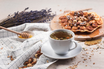Still life a cup of herbal tea on a tablecloth with honey, sweets and nuts