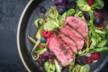 Traditional barbecue aged sliced fillet steak with lettuce and fruits as top view on a plate with...