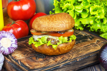 Appetizing burger on a wooden board against a background of vegetables