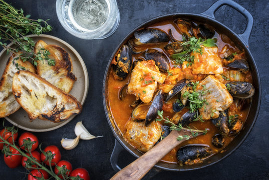 Traditional French Corsican fish stew with mussels and garlic baguette as top view in a pot