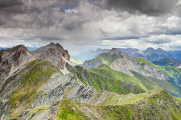 Rain shaft hits Karnischer Hohenweg path on zigzagging main ridge of Alpi Carniche Karnische Alpen range covered by rocks and grass, Italian Austrian border Belluno Veneto Osttirol Europe