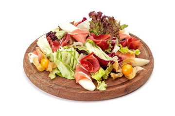 Meat cutting mixed up with lettuce leaves, cape gooseberry and arugula lies on a round wooden chopping board.