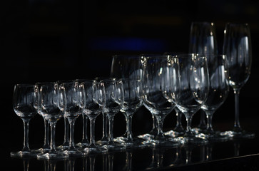 Rows of the empty wineglasses and empty glasses for vodka, going to unsharpness, stands on a black surface bar counter. 