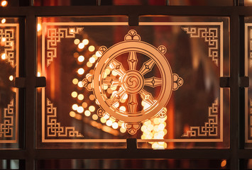 One of 8 Buddhist good symbols - a wheel of the teaching "Dharmachakra" against the background of fires of ritual candles.