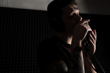 A portrait of a guy singing in front of a microphone on the counter, pressing it to his lips.