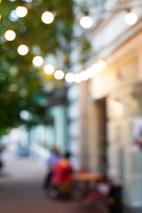Blurred view of street cafe lights, decorative garland with lights on the tree. Restourant terrace.