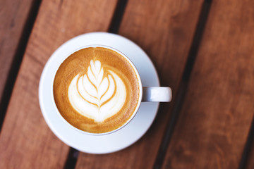 A cup of coffe with latte art on wooden table. Top view, morning mood, italian cappuccino.