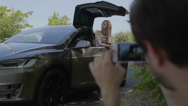 Young man make photo of his girl near the luxury car