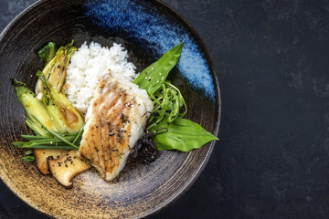 Modern Japanese fried cod fish filet with bok choi and rice as top view in a bowl with copy space right