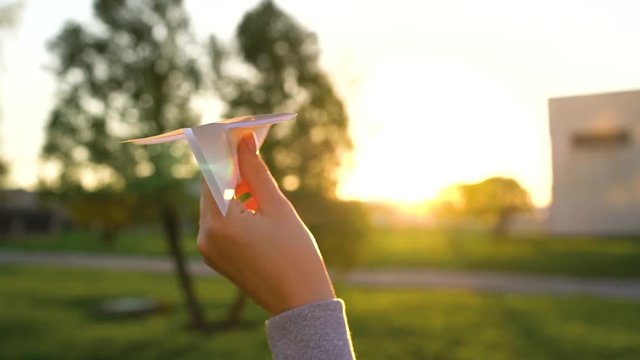 Hand launches paper airplane against sunset background. Slow motion