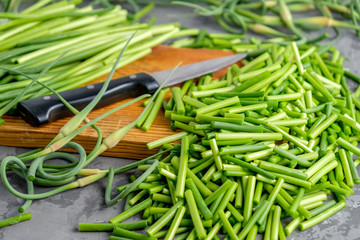 Healthy vegetarian seasonal food. Arrows young  fresh garlic chopped into many slices on a light wooden cutting board on grey concrete background. Closeup view