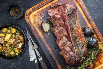 Traditioneller Barbecue Rehrücken mariniert mit Bratkartoffel und Pilzen als Draufsicht auf einem Schneidebrett 