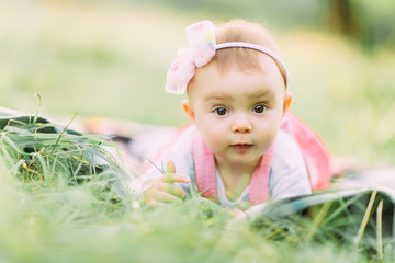 Portrait of happy joyful child in pink dress over green grass background. Happy little baby girl in the park. Family concept