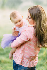 Young mother holding daughter in her arms. Beautiful Mother And Baby outdoors. Nature. Beauty Mum and her Child playing in Park together. Outdoor Portrait of happy family. Joy. Mom and Baby