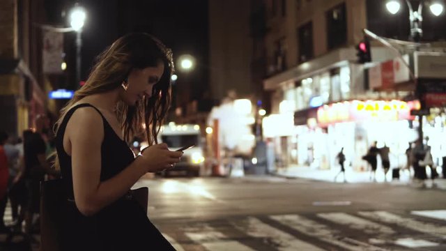 Young happy woman standing in crowded downtown, near the traffic road in New York, America and using the smartphone.