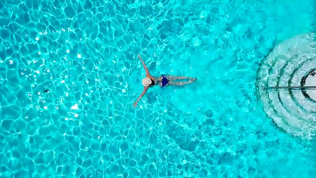 View from the top as a woman in a blue swimsuit swims in the pool
