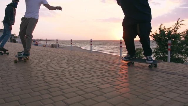 Group of young people skateboarding on the road in the early morning near the sea, close up shot