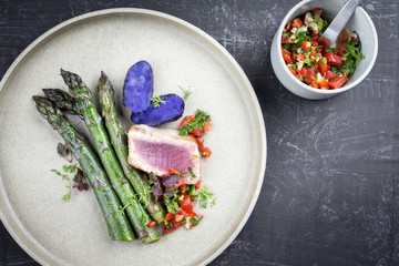 Modern fried tuna fish filet with green asparagus blue potatoes und vegetable chili relish as top view on a plate with copy space right