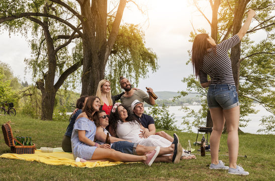 freunde machen ein gruppenfoto. brünette frau fotografiert ein selfie mit freunden. lifestyle picknick und grillen im park am see.