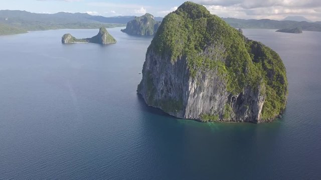 Aerial drone view flying over a sandy beach towards towering limestone karsts in an archipelago