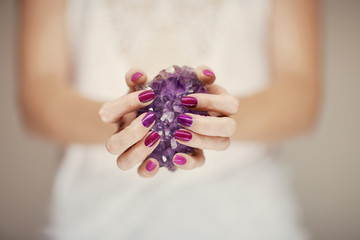Beautiful woman hands with perfect pink nail polish holding violet amethyst crystal, can be used as background - obrazy, fototapety, plakaty