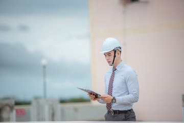 smiling young architect or engineering builder in hard hat with tablet over group of builders at...